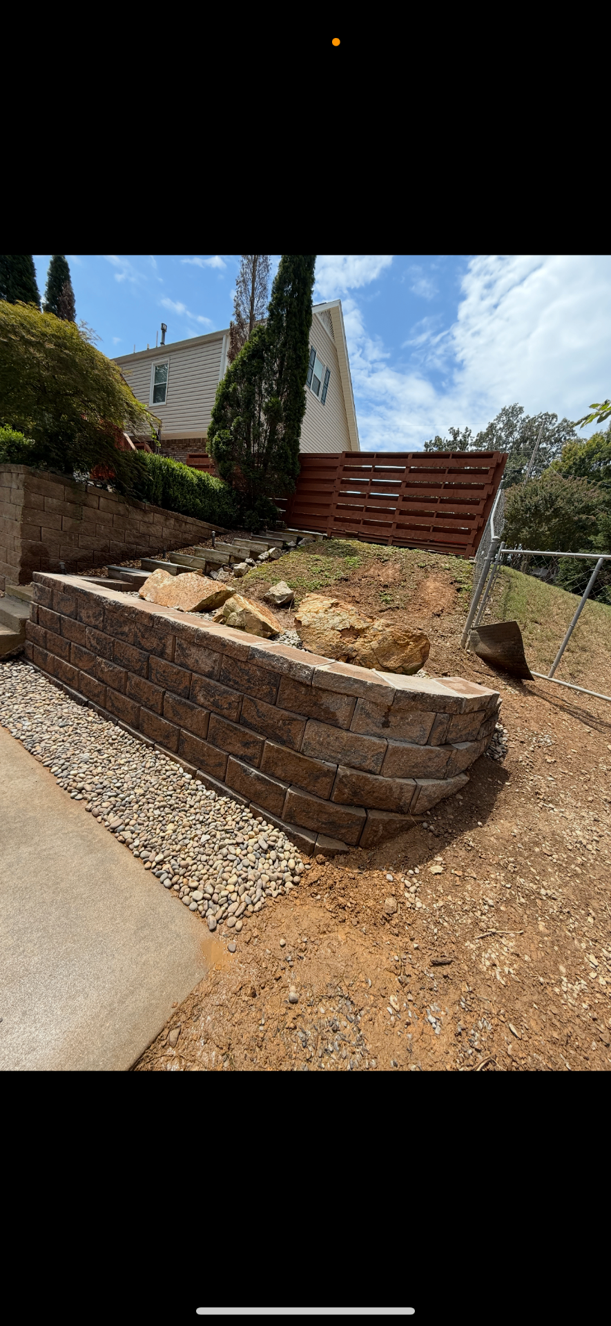 Curved brown retaining wall with steps and decorative river rock